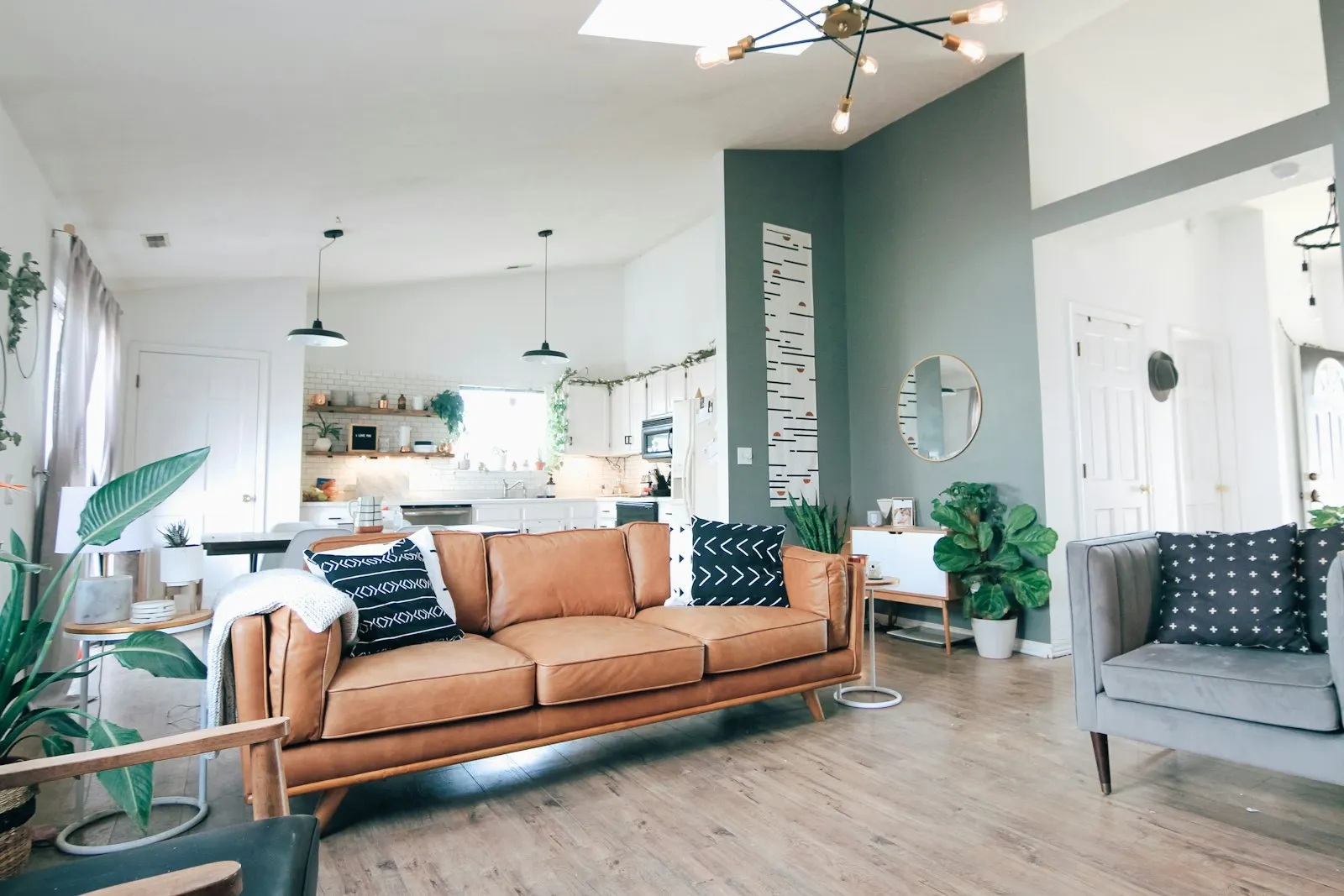 Teal feature wall behind a tan leather sofa with a brass floor lamp and gallery frames