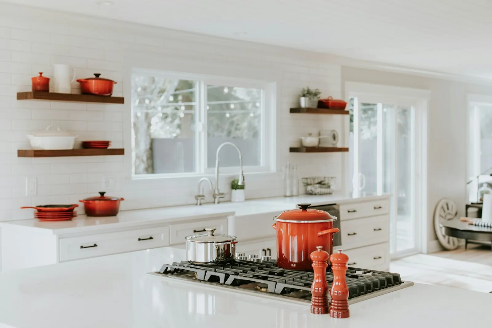 White kitchen with open shelving, red accents and a farmhouse sink under the window